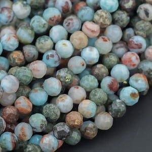 May include: A close-up of a collection of round beads in various colors, including shades of blue, green, brown, and orange. The beads have a faceted surface and are strung together, suggesting they are for jewelry making.