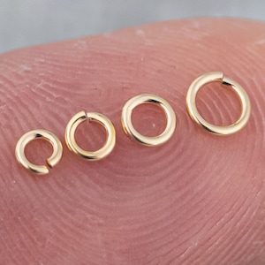 May include: Four gold jump rings of different sizes, arranged in a row from largest to smallest.