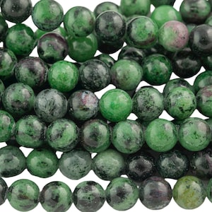 May include: A strand of green, black, and white gemstone beads. The beads are round and have a speckled appearance.