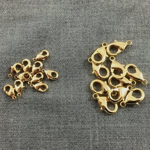 May include: A close-up of two groups of gold-toned lobster clasps. The larger group has 10 clasps, and the smaller group has 12 clasps.