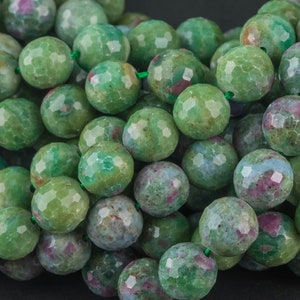 May include: A strand of green, faceted gemstone beads with pink and blue inclusions. The beads are round and have a slightly irregular shape.