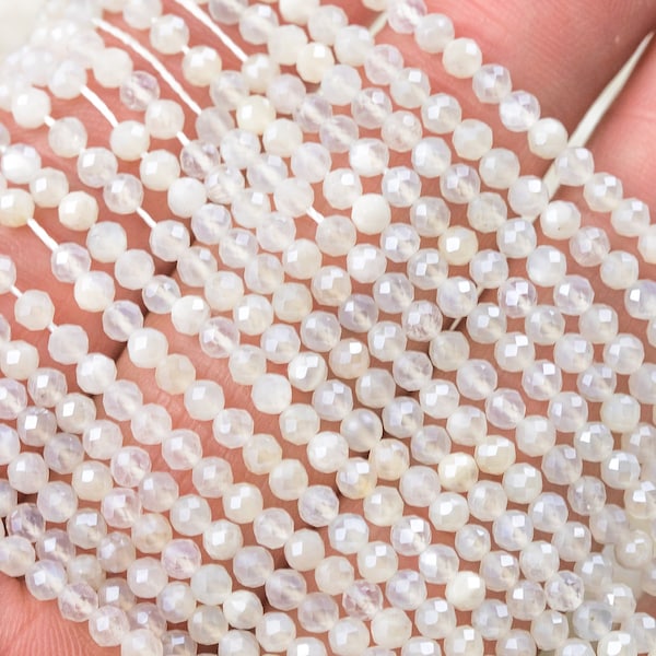 May include: A strand of white moonstone beads, faceted and round, strung on a white thread. The beads are approximately 4mm in diameter.