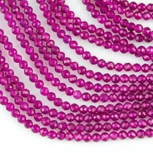 Może przedstawiać: Zbliżenie na wiele pasm małych, fasetowanych, magentowych koralików. Koraliki są nanizane razem, tworząc warstwowy efekt na białym tle. Koraliki te nadają się do tworzenia biżuterii.