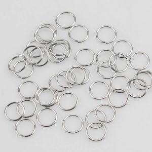 May include: A pile of silver jump rings, a type of metal ring used for jewelry making.