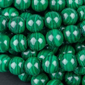 Op de afbeelding: Een streng groene malachiet kralen. De kralen zijn rond en hebben een gladde, gepolijste afwerking. De malachiet is een natuursteen met een kenmerkende groene kleur en draaiende patronen.