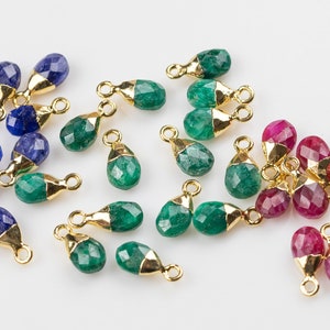 May include: Assortment of gemstone teardrop charms with gold-plated jump rings. The charms are in shades of blue, green, and red.