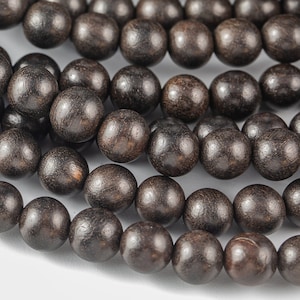 May include: A close-up of a strand of dark brown wooden beads. The beads are round and smooth, and they are strung together in a long strand.
