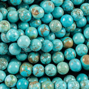 May include: A strand of turquoise beads, each bead is a round, smooth, and has a mottled blue and brown color.