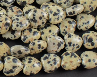 May include: A strand of dalmatian jasper heart-shaped beads. The beads are a light beige color with black spots.
