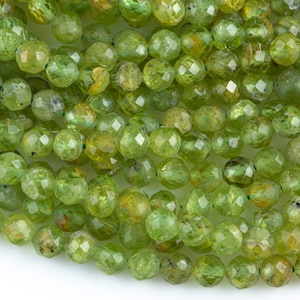 May include: A strand of green peridot beads, faceted and round, with a slight golden hue. The beads are strung on a clear thread and are ready for jewelry making.