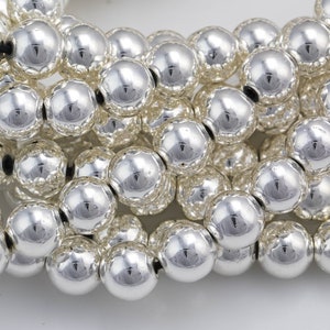 May include: A strand of silver-toned round beads. The beads are smooth and shiny, and they are arranged in a close-up view.