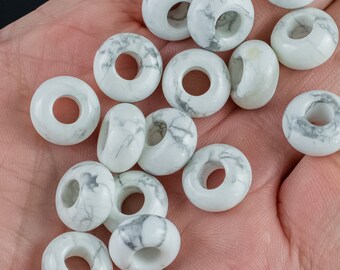 Könnte beinhalten: Eine Sammlung weißer Howlith-Donut-Perlen mit grauen Adern. Die Perlen sind auf einer Hand zu einem Haufen angeordnet.