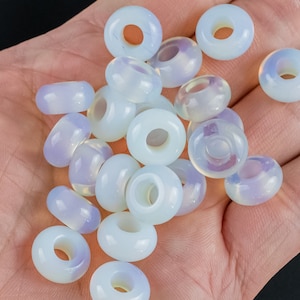 May include: A pile of white opal beads with a hole in the center of each bead. The beads are iridescent and have a milky white color.