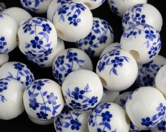 Könnte beinhalten: Weiße Keramikperlen mit einem blauen Blumenmuster. Die Perlen sind rund und haben ein Loch in der Mitte zum Auf fädeln.