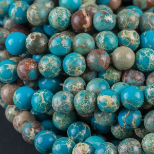 May include: A strand of blue and brown jasper beads. The beads are round and have a speckled pattern.