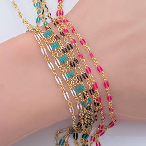 Puede incluir: Collares de cadena dorados con detalles de esmalte de colores en turquesa, rosa, negro y blanco. Los collares están superpuestos, creando un accesorio vibrante y elegante. Las cadenas son delicadas y presentan un diseño de eslabones ovalados.