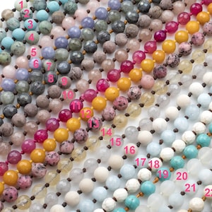 May include: A close-up of 25 strands of beads, each strand is a different color and type of stone. The strands are laid out in a row, with the numbers 1 through 25 written next to each strand.
