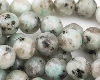 Puede incluir: Una hebra de cuentas redondas de piedra preciosa verde y blanca moteadas. Las cuentas tienen una textura rugosa y facetada.