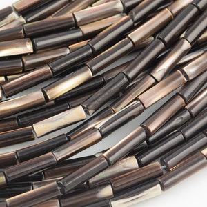 Puede incluir: Una hebra de cuentas de concha marrón e iridiscente, cada cuenta es un cilindro largo y delgado.