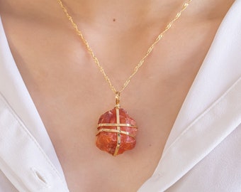 May include: A gold chain necklace with a pendant featuring a red, orange, and brown crystal encased in a gold wire cage.