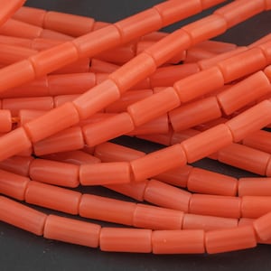 May include: A close-up of a strand of coral beads. The beads are a bright orange color and are cylindrical in shape. The beads are strung together on a clear thread.