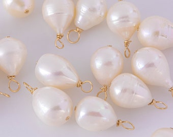 May include: A collection of white teardrop-shaped pearls with gold wire loops. The pearls are scattered on a white surface.