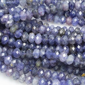 May include: A strand of blue faceted gemstone beads. The beads are round and have a slightly irregular shape. They are a light to medium blue color with a slight shimmer.