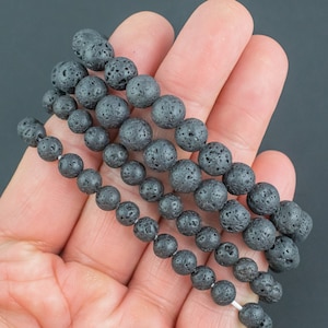 May include: Four strands of black lava rock beads of varying sizes, held in a hand.