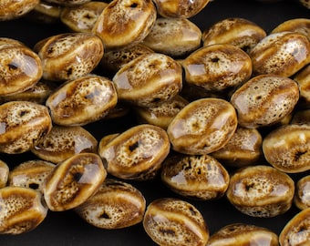 May include: A strand of brown ceramic beads with a speckled pattern. The beads are oval shaped and have a glossy finish.