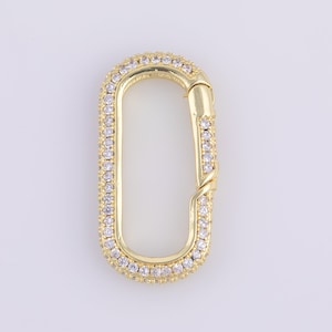 May include: Gold-colored oval carabiner clasp, encrusted with small, clear crystals. The clasp has a hinged opening and a secure closure. The crystals are set around the perimeter of the oval, adding sparkle and detail to the jewelry component.
