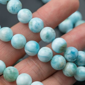 May include: A strand of light blue and white seafoam jasper beads. The beads are round and have a smooth, polished finish.