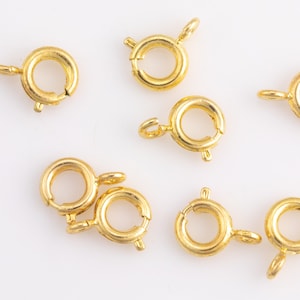 Può includere: Otto anelli di salto in metallo dorato con chiusura a molla. Questi anelli sono comunemente usati per la creazione di gioielli e l'artigianato.