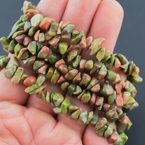 May include: A strand of green, red, and brown gemstone chips. The chips are irregularly shaped and have a natural, rough texture.