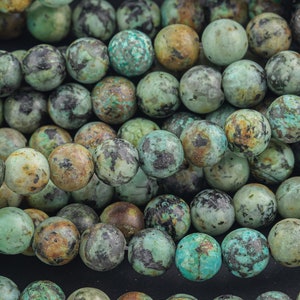 May include: A close-up of a strand of round, green turquoise beads with brown and black markings. The beads are smooth and polished.