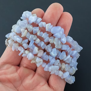 Puede incluir: Una hebra de cuentas de ágata en forma de chip de color azul claro y blanco. Las cuentas están enhebradas en un hilo transparente.