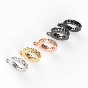 May include: Five different coloured metal rings with a row of clear crystals around the edge. The rings have a small loop at the top for attaching to a chain or other jewellery.