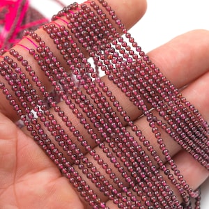 May include: A strand of deep red garnet beads, approximately 4mm in diameter, strung on a thin thread. The beads are smooth and polished, with a slight sheen.