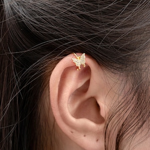 May include: A gold butterfly ear cuff with clear rhinestones. The ear cuff is worn on the upper part of the ear.