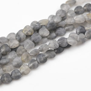 May include: A strand of gray and clear heart-shaped gemstone beads. The beads are strung on a clear thread and are arranged in a random pattern.