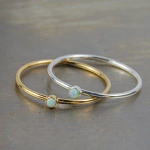 May include: Two simple rings with a single opal gemstone on each. One ring is gold and the other is silver.
