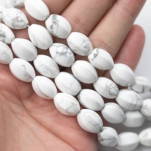 May include: A strand of white oval-shaped howlite beads with gray veining. The beads are smooth and polished.