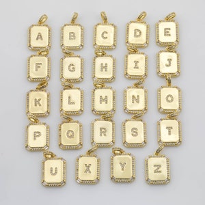 May include: A set of 26 gold-tone pendants, each featuring a different letter of the alphabet. The pendants are rectangular in shape and have a sparkly finish. Each pendant has a small loop at the top for attaching to a chain.