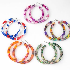 Può includere: Cinque paia di orecchini a cerchio colorati e con motivi. Ogni paio è realizzato con un cerchio spesso in plastica marmorea. Gli orecchini sono disponibili in una varietà di colori, tra cui rosa, blu, rosso, arancione e verde.