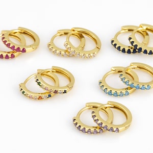 May include: Set of gold hoop earrings with colorful gemstones. Each pair features a different color combination of gemstones, including red, blue, green, purple, and white.