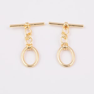 May include: Two gold-toned metal toggle clasps with a round ring and a straight bar. The clasps are commonly used for jewellery making and crafting.