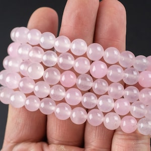 May include: A strand of pale pink rose quartz beads, stacked and held in a hand. The beads are smooth and round, with a subtle shine.