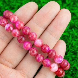 Pode incluir: Um bracelete de pedras preciosas rosa e vermelho com contas redondas. O bracelete é feito de pedras naturais e é perfeito para adicionar um toque de cor a qualquer roupa.