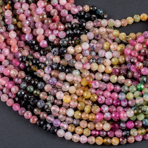 May include: A strand of faceted gemstone beads in shades of pink, green, black, and brown. The beads are round and have a slightly irregular shape.