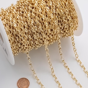 May include: A spool of gold-colored chain with oval links. The chain is wound around a white plastic spool. A penny is next to the chain for size comparison. The chain is likely used for jewelry making or other crafts.