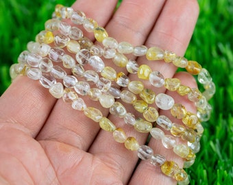 Puede incluir: Una hebra de múltiples hebras de cuentas de piedras preciosas transparentes y amarillas, probablemente citrino, en una mano.